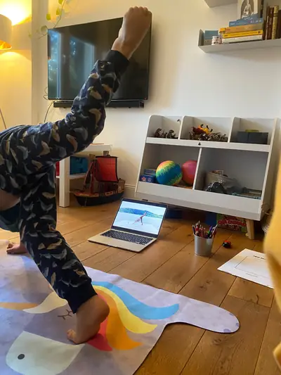 Ein Kind streckt im Wohnzimmer ein Bein hoch, vor ihm der Laptop