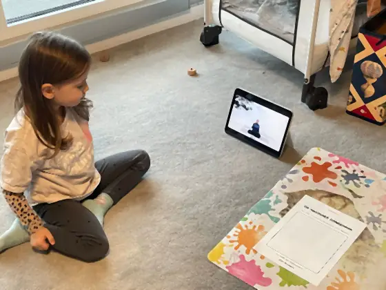 Ein Mädchen sitzt vor dem Tablet, daneben liegt das Ausmalblatt