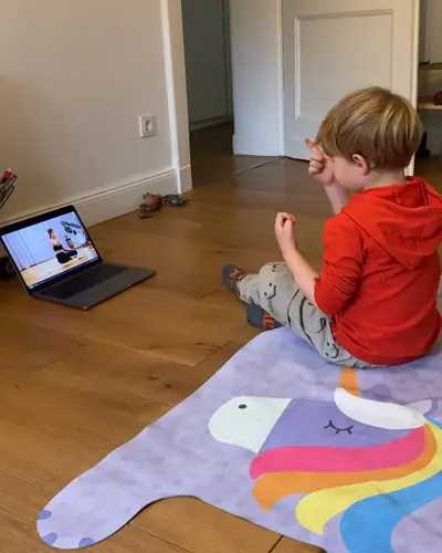 Ein Junge sitzt auf seiner Einhorn-Matte und macht die Übung vom Laptop nach